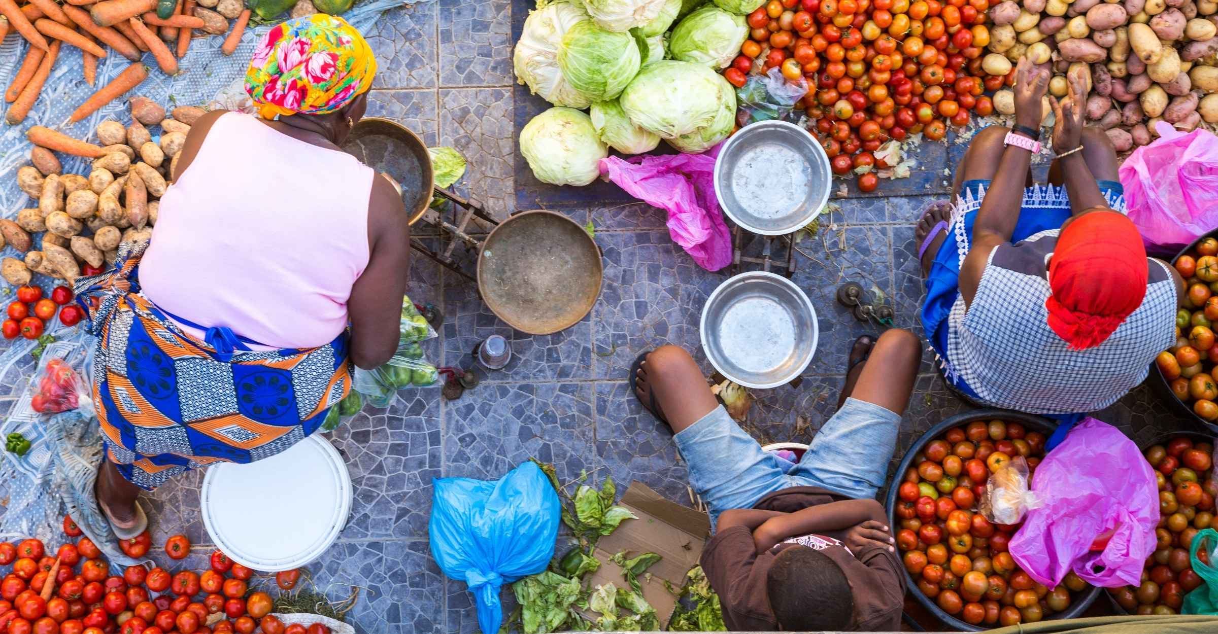 Aerial view of a busy African produce market, traders and customers gathered around stalls of vegetables.
